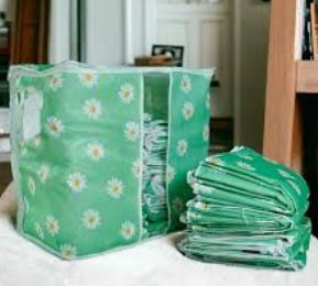 Green daisy print fabric storage bag filled with folded blankets, featuring a clear front window for easy viewing.